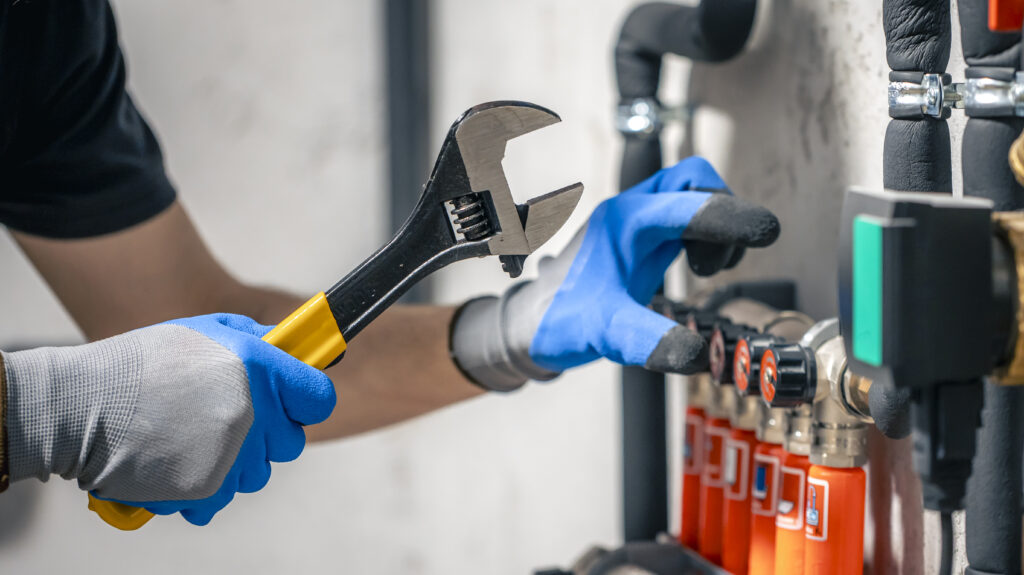 A man installs a heating system in a house and checks the pipes with a wrench. Adjusting heating valves in a residential building. A plumbing and heating technician works.